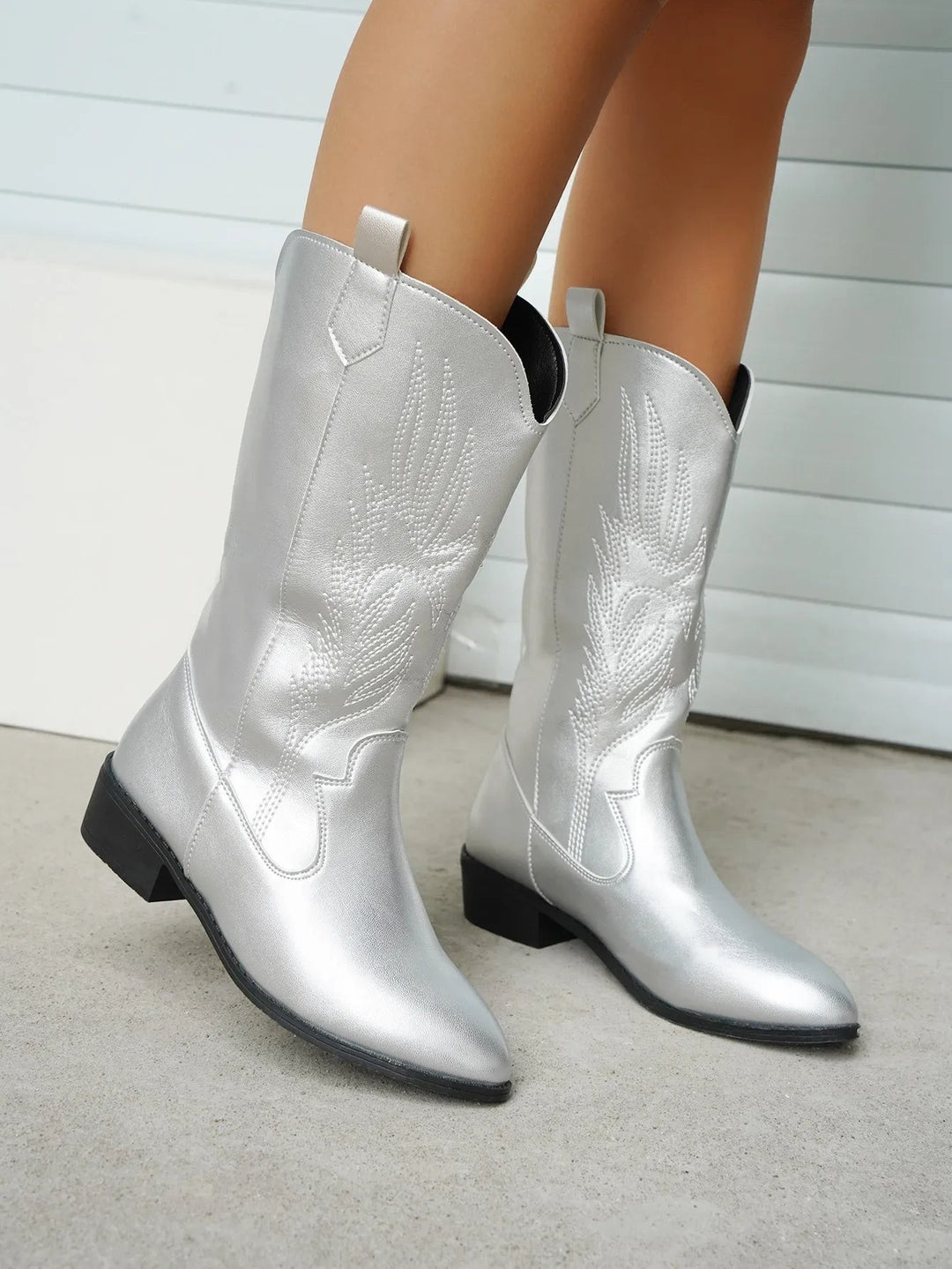 Silberne Cowboystiefel mit floraler Stickerei an schlanken Beinen