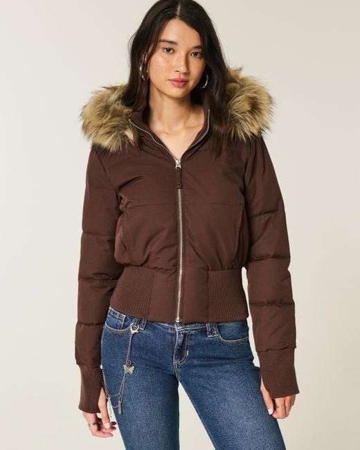 Braune Pufferjacke mit Kapuze und Kunstfellbesatz, kombiniert mit Jeans