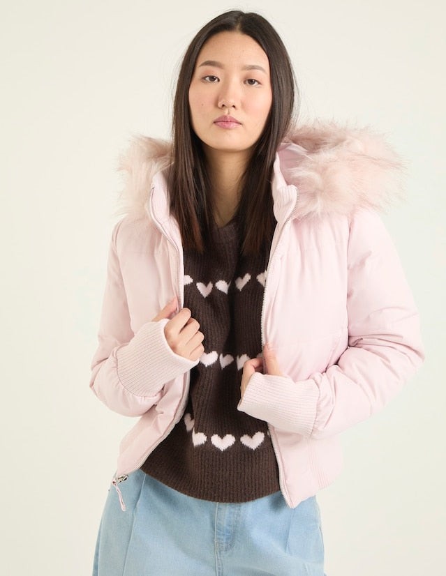 Rosa Pufferjacke mit Kunstfellkapuze, offen getragen über gemustertem Pullover