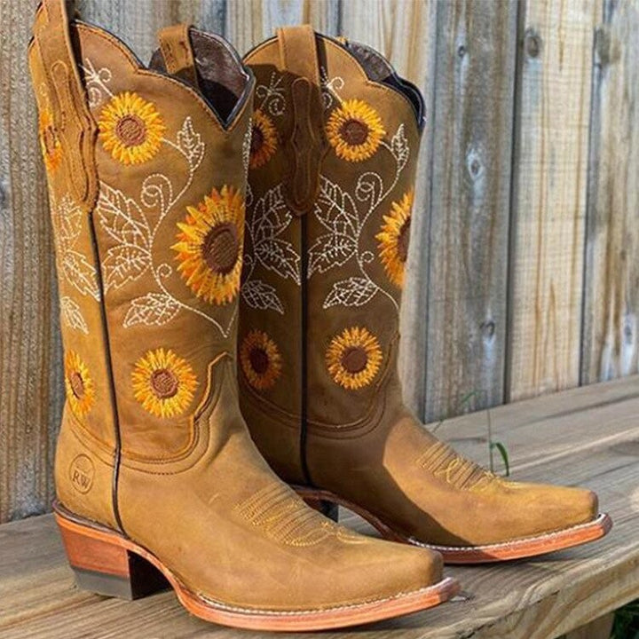 Cognacfarbene Cowboystiefel mit Sonnenblumenmuster auf Holzbank