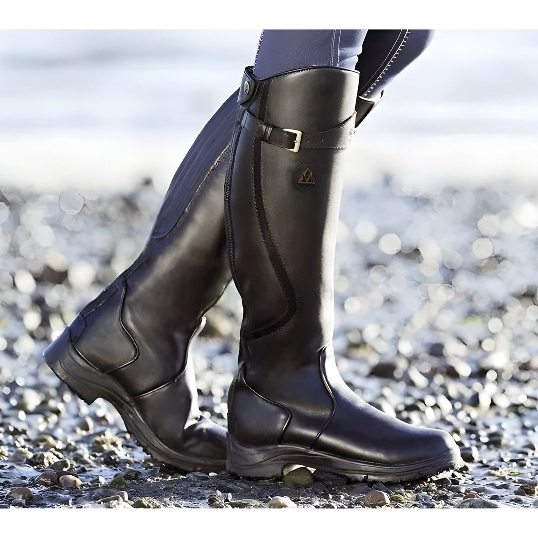 Schwarze Kniestiefel aus Leder mit Schnalle, am Kiesstrand getragen