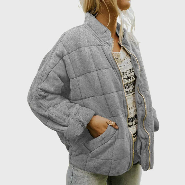 Graue Steppjacke mit Stehkragen, lässig getragen über gemustertem Pullover