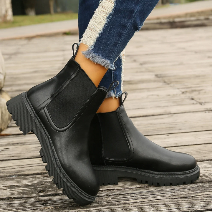Schwarze Lederstiefel mit Zugschlaufen und grober Sohle am Fuß