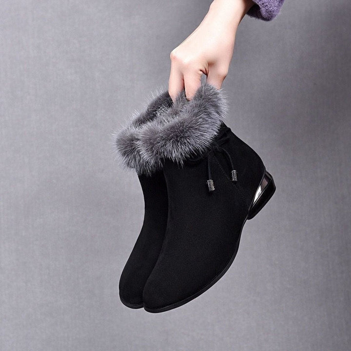 Schwarze Ankle Boots aus Wildleder mit grauem Kunstfellbesatz, in der Hand gehalten