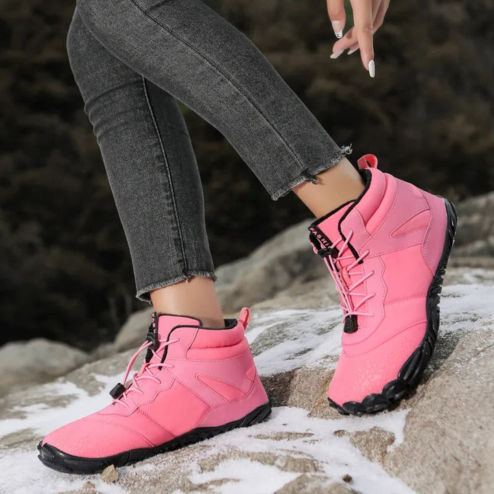 Pinke Barfuß Winterschuhe an Frau getragen auf schneebedecktem Fels
