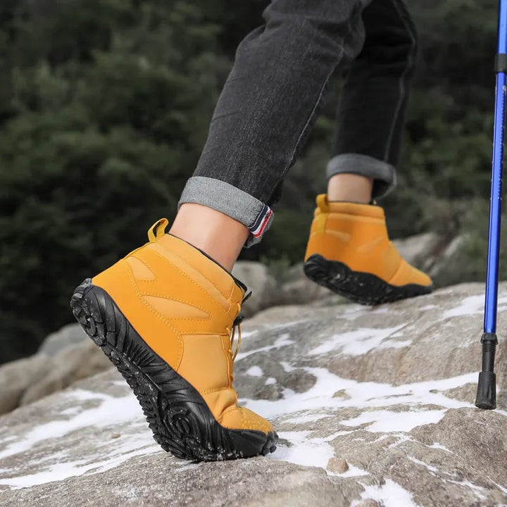 Gelbe Winterstiefel mit Wanderstock beim Aufstieg über verschneite Felsen