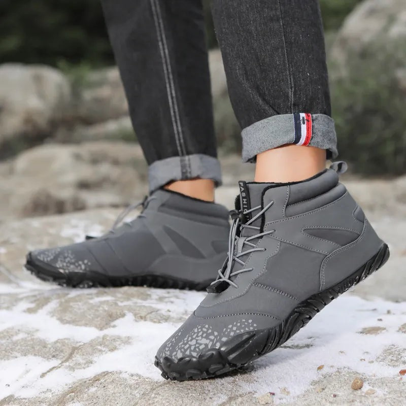 Graue Winterschuhe mit Profilsohle beim Gehen auf verschneitem Felsen