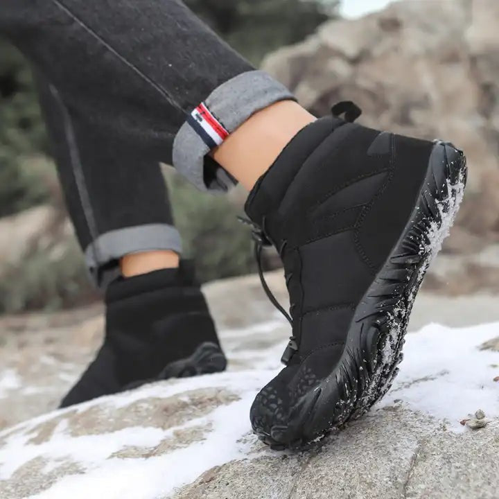 Schwarzer Winterschuh mit griffiger Sohle beim Schritt über Felsen