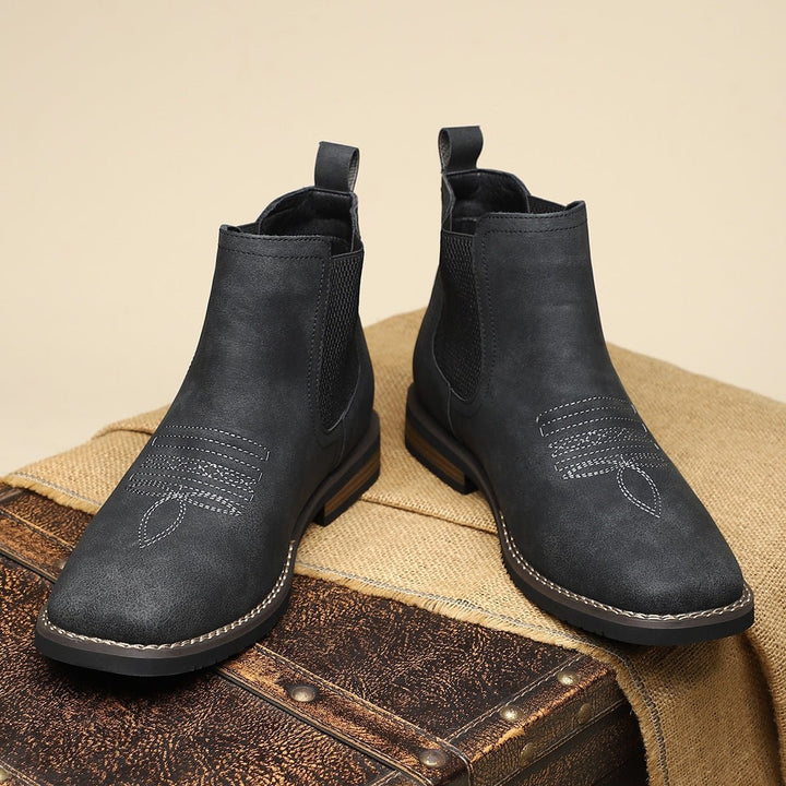 Schwarze Stiefeletten paarweise auf Jute-Stoff mit Vintage-Koffer