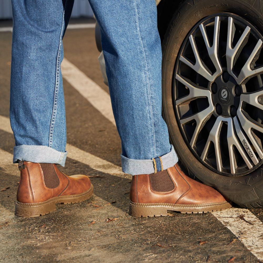 Braune Herren-Chelsea-Boots kombiniert mit umgeschlagener Jeans am Fahrzeugreifen